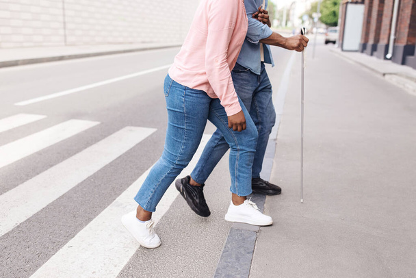 Неузнаваемая молодая чернокожая женщина помогает парню с нарушением зрения переходить городскую улицу, копирует пространство - Фото, изображение