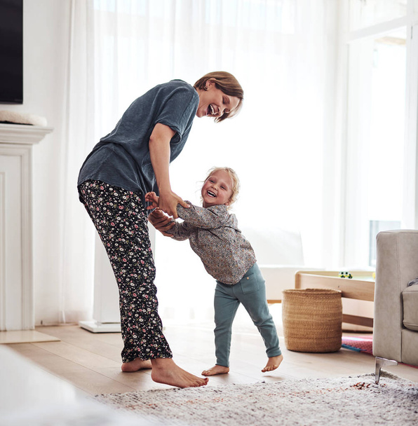 I want to dance with my mom. Full length shot of an attractive young mother and playing with her daughter in the living room at home. - Фото, зображення
