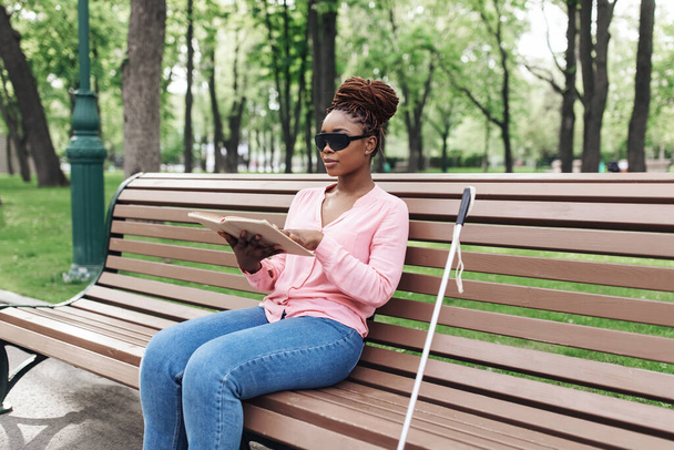 Joven mujer negra con discapacidad visual sentada en el banco en el parque de la ciudad, leyendo el libro Braille al aire libre, espacio para copiar - Foto, Imagen