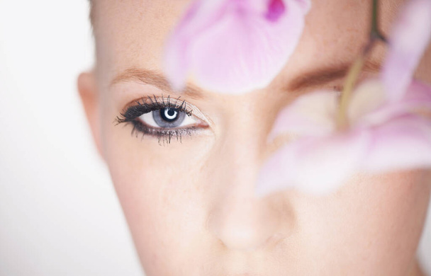 Vision of beauty. A beautiful young woman looking out from behind an orchid. - Foto, immagini