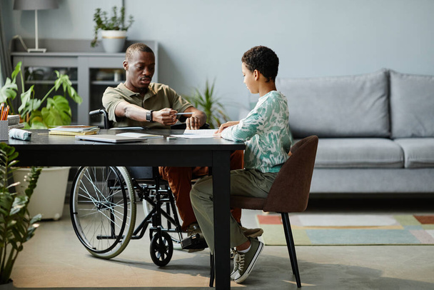 Hombre negro en silla de ruedas ayudando a su hija con la tarea - Foto, Imagen