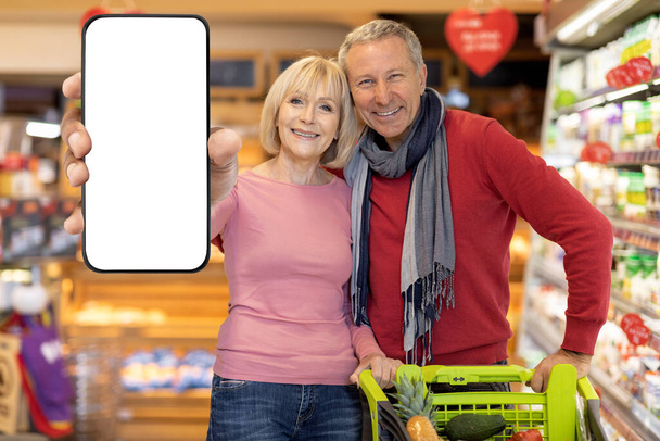 Αγαπώντας τα ηλικιωμένα ζευγάρια ψώνια στο σούπερ μάρκετ, δείχνει smartphone, mockup - Φωτογραφία, εικόνα