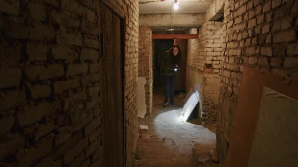 Een meisje in een verschrikkelijke staat doorzoekt een enge kelder om een mogelijke schuilplaats te vinden in het geval van een bomexplosie. Nieuws over spanningen tussen Oekraïne en Rusland. Russische agressie. De dreiging van oorlog. - Video