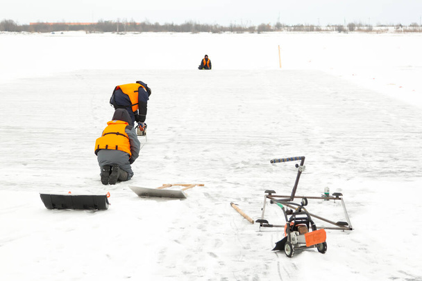 Trabajadores instaladores en chalecos salvavidas de color naranja en el hielo de un lago congelado en las marcas del hielo - Foto, Imagen