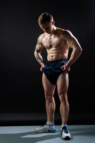 Homem no fundo preto mantém halteres bombeados na aptidão musculação peito exercício fisiculturista masculino Jovem metal, um ajuste músculos no tronco dos abdominais e pernas bíceps no crescimento do rolo - Foto, Imagem