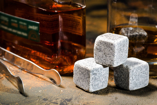 Cold whiskey stones next to a glass and a bottle. Soapstone for cooling whiskey. Close-up. - Foto, afbeelding