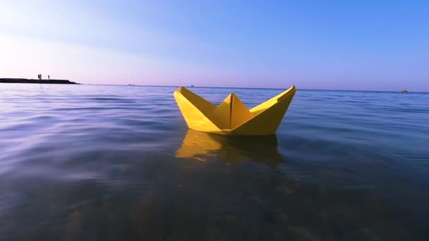 Barca di carta gialla galleggia sulla superficie di onde d'acqua blu del mare primo piano. - Filmati, video