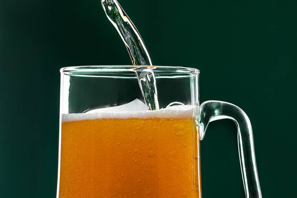 A sör zöld hátterű bögrébe ömlik. Szent Patrik napját ünnepeljük. Hagyományos ír ital. - Fotó, kép