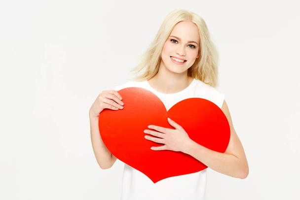 Feliz y enamorada. Una hermosa joven sosteniendo un corazón rojo sobre un fondo blanco. - Foto, imagen