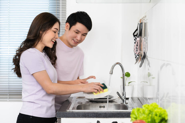 happy young couple washing dishes together in the sink in the kitchen at home - Photo, Image