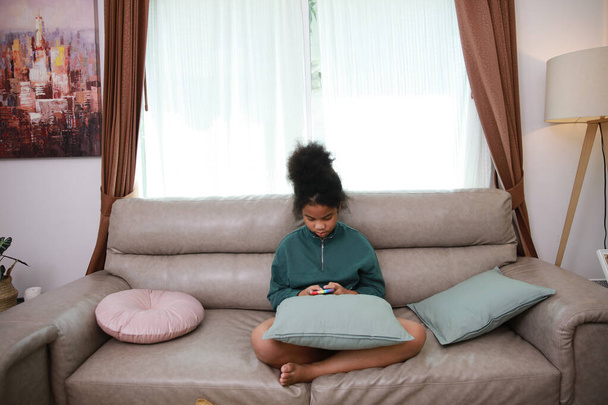 Young little girl concentrate on mobile phone on sofa at home , lifestyle of children with mobile , Nomophobia symton - Foto, imagen