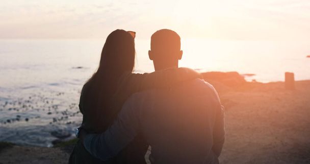 Estes são os momentos que tornam seu vínculo mais forte. Foto retrovisada de um casal afetuoso irreconhecível assistindo ao pôr do sol na praia. - Foto, Imagem