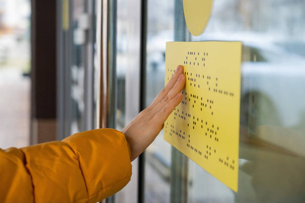 Close-up of a woman reading a braille lettering on a glass door. - Photo, image