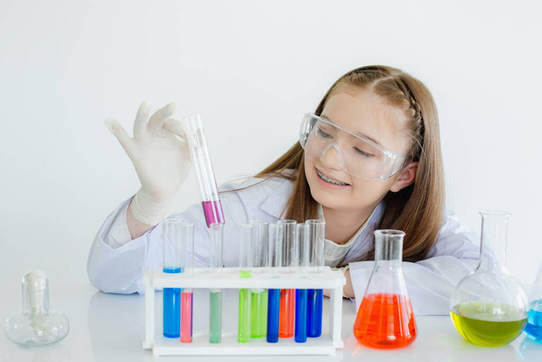 Studenti di scienze infantili studiano esperimenti chimici liquidi in una stanza di laboratorio bianca. scolaretta in possesso di provetta con l'apprendimento della biotecnologia. educazione scientifica cocept. - Foto, immagini