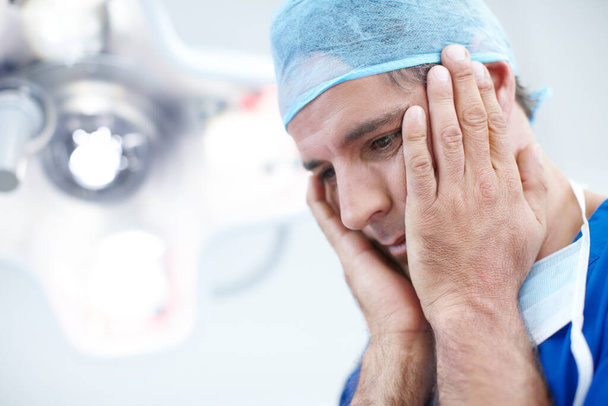 How do I tell the family. Close-up a doctor looking somewhat distraught holding his head in his hands. - Photo, Image