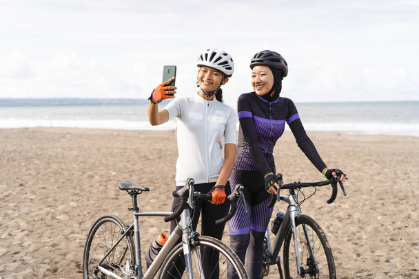 muslim woman cyclist taking selfie photo together at the beach - 写真・画像