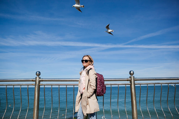 blondynka z plecakiem na tle zimnego morza, mewy na niebie. koncepcja podróży, podróży, imigracji - Zdjęcie, obraz