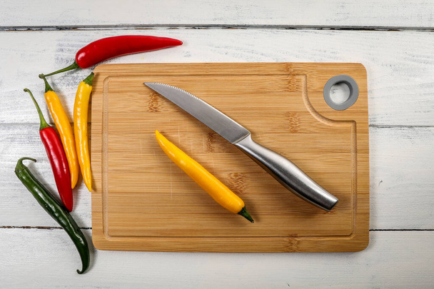 Colored pepper and a knife on a bamboo cutting board - Zdjęcie, obraz