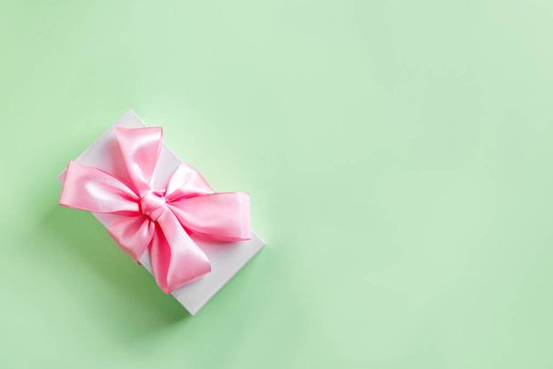 Gift box with pink silk ribbon and bow on green pastel background, top view, copy space. Celebration mother's day or birthday concept. - Φωτογραφία, εικόνα