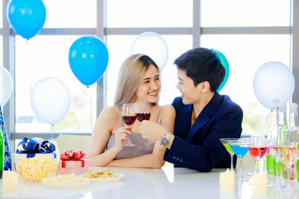 Молода подружня пара азіатських коханок у формальному костюмі і красива дружина посміхаються, тримаючи високі склянки вина тости разом на щасливій новорічній вечірці на декорованому напої і за столом.. - Фото, зображення
