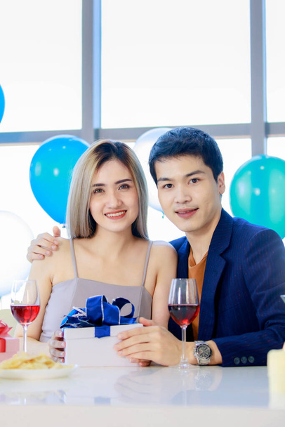 Millennial joven amante pareja asiática marido en traje formal y hermosa esposa sonriendo sosteniendo vasos altos vino brindis juntos en feliz fiesta de año nuevo en la mesa de bebidas y alimentos decorados. - Foto, Imagen