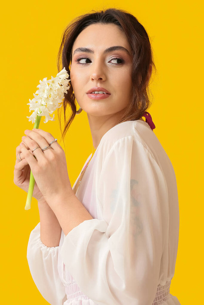Sarı arka planda sümbül çiçekleri olan güzel genç bir kadın. - Fotoğraf, Görsel