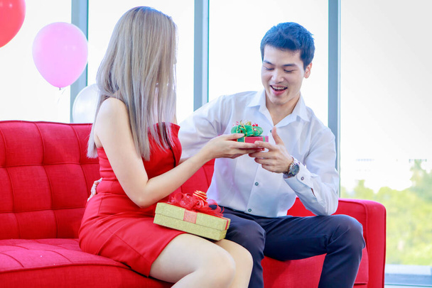 Тысячелетний молодой азиатский любовник пара красивый парень и красивая девушка сидя на уютном диване улыбаясь смеясь обмениваясь unboxing подарок коробки вместе отмечая годовщину знакомства. - Фото, изображение