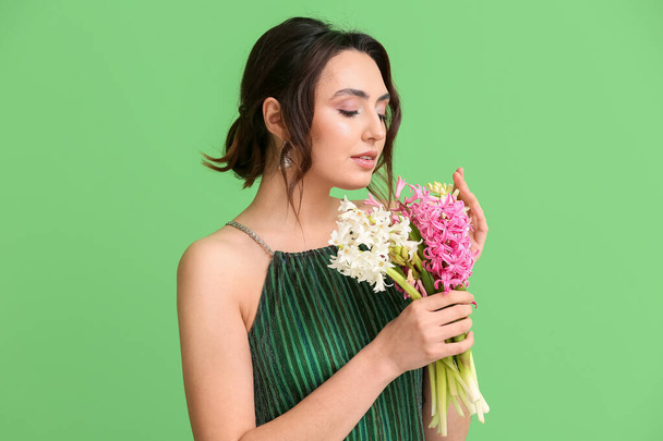 Όμορφη νεαρή γυναίκα με λουλούδια υάκινθος σε πράσινο φόντο - Φωτογραφία, εικόνα