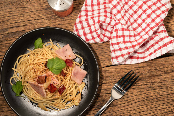 Pasta espaguetis ajo jamón chile seco en plato negro aislado sobre fondo de madera de cerca, vista superior, concepto de alimentos. - Foto, Imagen