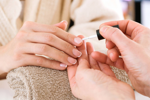 Crop anonymous manicure master applying nail polish to customer in bathrobe during beauty procedure in salon - Photo, Image