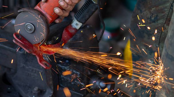 Genç işçiler metal öğütücüleri kullanır. Metal öğütücüden güzel turuncu parıltılar tasarlamak ve modifiye etmek için bir motosikletin çelik parçalarını.. - Fotoğraf, Görsel