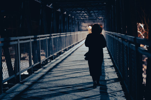 silhouette of a man in a black dress with a backpack on the background of the bridge - Foto, Imagem