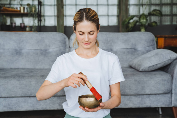 A cute girl holds a Tibetan singing bowl in her hands. Therapeutic sound of high frequencies and vibrations from bowls. Meditating girl. High quality photo - Foto, afbeelding
