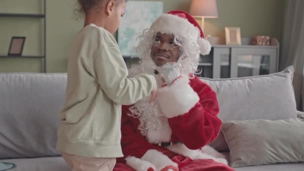 Közepes lassú aranyos afro-amerikai 8 éves lány játszik apával piros jelmezben a Mikulás leveszi a kalapját és szakáll töltik karácsonyi ünnepek együtt otthon - Felvétel, videó