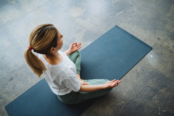 A shot above of a girl meditating on a yoga mat. Sit in the lotus position and think. The girl is engaged in yoga, the search for harmony and serenity. High quality photo - Fotó, kép