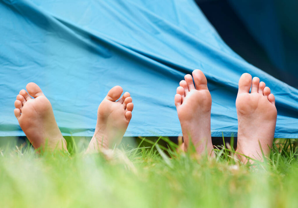 Paljain jaloin retkellä. Matala kulma näkymä kaksi lasta makaa paljain jaloin teltan alla. - Valokuva, kuva