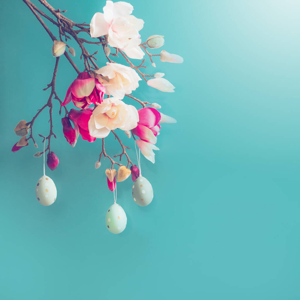 Hanging Easter eggs on magnolia spring blossom at blue  background, top view - Fotó, kép