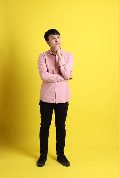 The Asian man with pink shirt standing on the yellow background. - Valokuva, kuva