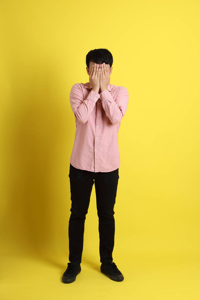 Azjata w różowej koszuli stojący na żółtym tle. - Zdjęcie, obraz