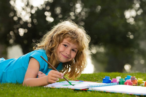 Lapsi poika maalaus maaleilla väri ja harja puistossa ulkona. Lasten harrastus, onnellinen lapsuus. - Valokuva, kuva