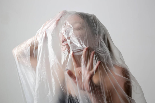 Woman wrapped in plastic sheet. Studio shot. Woman and mental health concept. - Фото, изображение