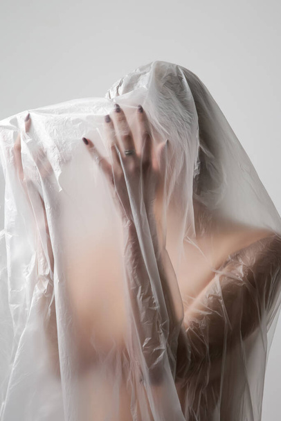 Woman wrapped in plastic sheet. Studio shot. Woman and mental health concept. - 写真・画像