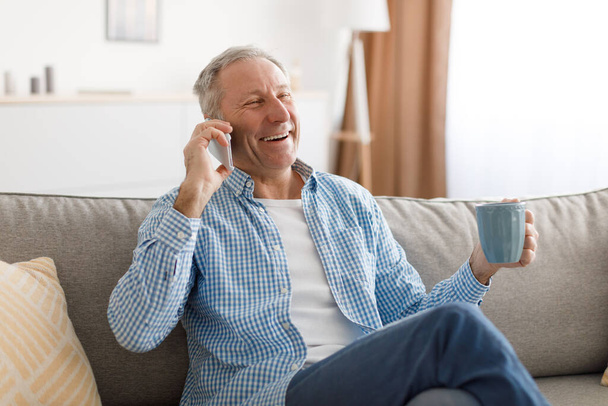 Vrolijke volwassen man praten op mobiele telefoon zitten op de bank - Foto, afbeelding