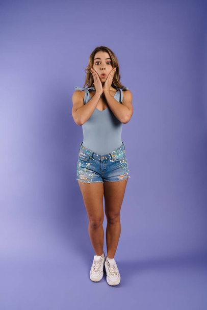 Shocked young white woman wearing denim shorts standing isolated over blue wall background - Fotografie, Obrázek
