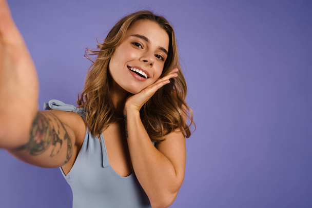 Young white woman smiling and taking selfie photo isolated over purple background - Foto, afbeelding