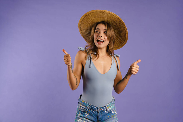Young white woman in straw hat gesturing thumbs up isolated over purple background - Foto, immagini