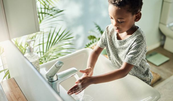 子供たちは石鹸と水で頻繁に手を洗うべきです。自宅のバスルームでタップで手を洗う男の子の高角度ショット. - 写真・画像