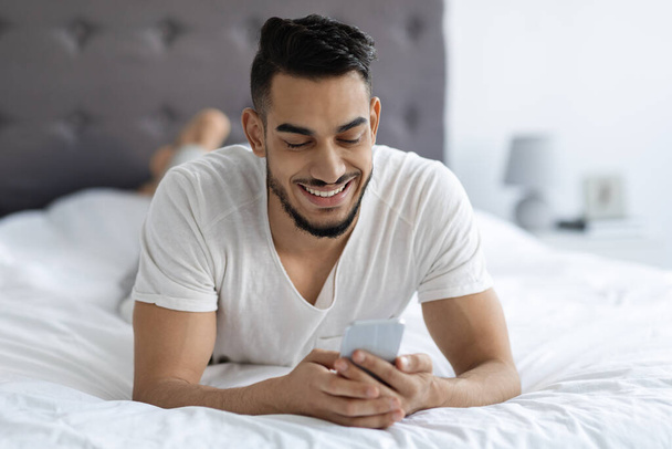 Portrait de beau jeune homme arabe se reposant au lit avec Smartphone - Photo, image