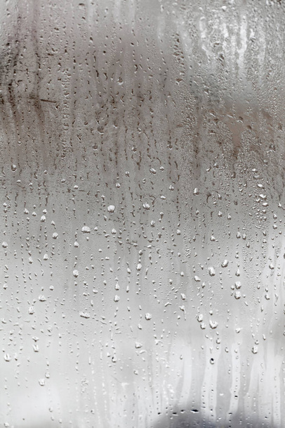 Condensación en vidrio con gotas que fluyen hacia abajo, fondo natural vertical, humedad y niebla en blanco. Afuera, mal tiempo, lluvia - Foto, imagen