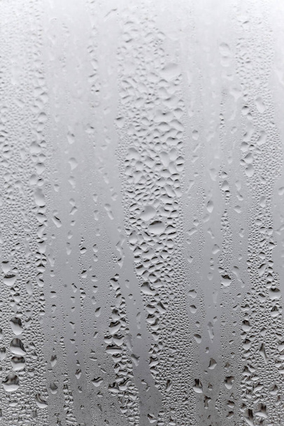 Condensación de agua sobre fondo de cristal de ventana. Afuera, mal tiempo, lluvia, humedad y niebla en blanco. Fondo natural vertical - Foto, Imagen